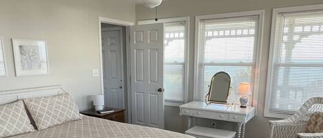 A bedroom with a bed, a vanity with a mirror, a chair, and a ceiling fan.