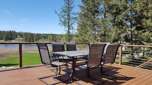 Um terraço com mesa e cadeiras, com vista para a água e uma área arborizada.