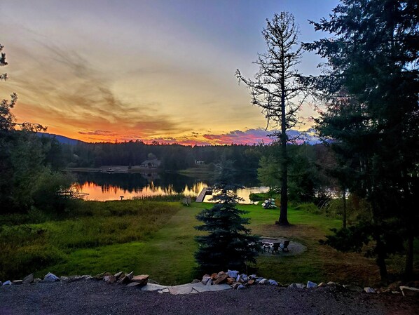 A lakeside view with a clear sky, a grassy area with a picnic table, and a small dock extending into the water. - Waterfront AND only 30 min to Schweitzer! Hot Tub, Movie Theater Room! (Sagle)