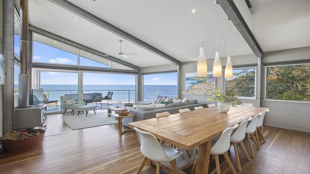 A spacious living area with a large wooden table, white chairs, and a sofa. There is a large window offering a view of the ocean. - the nest at killcare (Killcare)