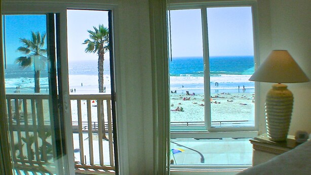 Habitación con vista a la playa, una palmera y una lámpara sobre una mesa.