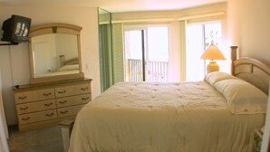 Un dormitorio con cama, cómoda, espejo y televisor sobre una estantería.
