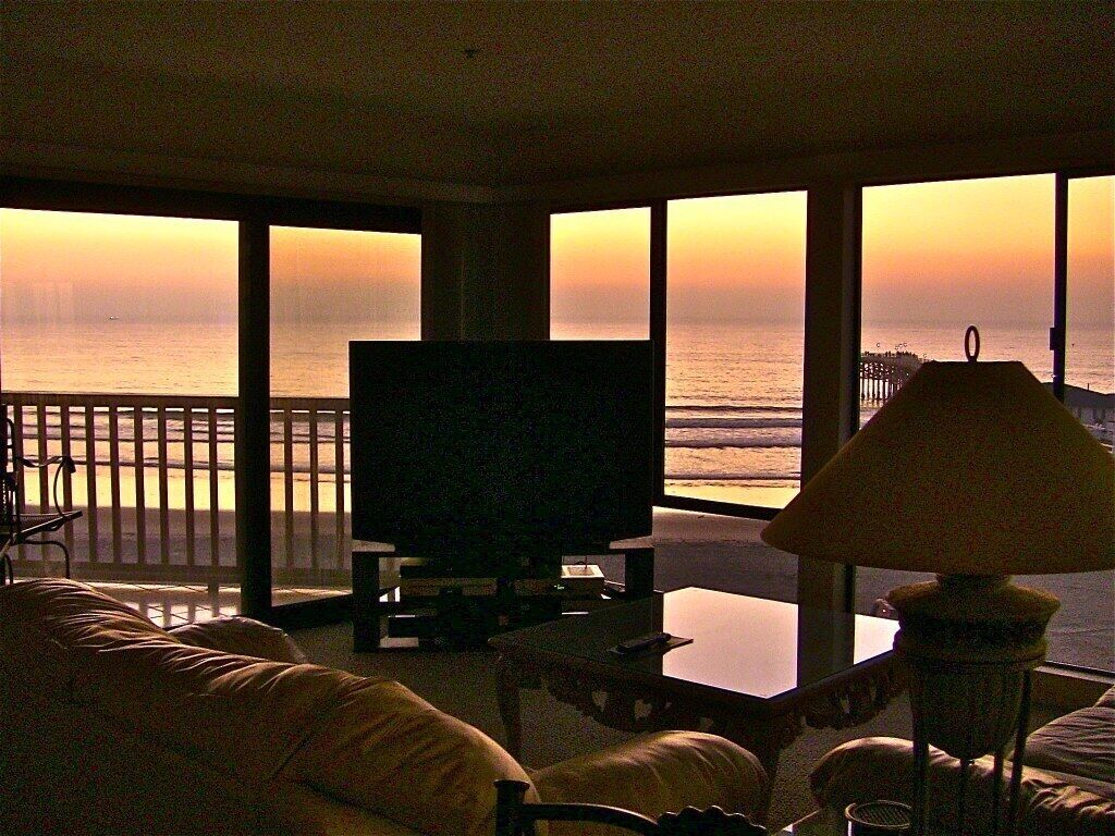 A living room with a TV, a lamp, and a view of the ocean at sunset.