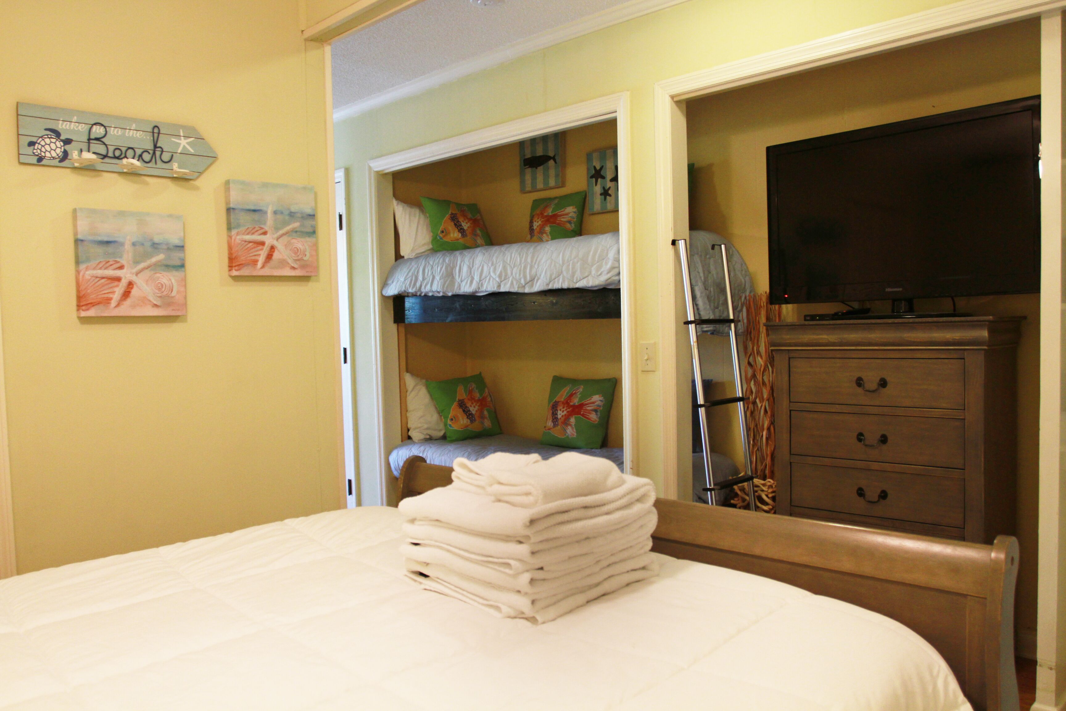 Un dormitorio con una cama litera, un televisor, un aparador y obras de arte en las paredes.