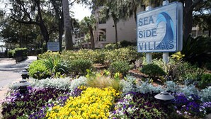 Schild für Sea Side Villas mit Garten und verschiedenen Blumen.