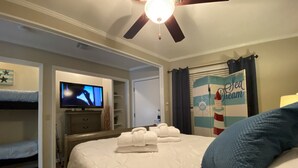 Ein Hotelzimmer mit Bett, Fernseher, Deckenventilator und einer Wand mit einem maritimen Poster.