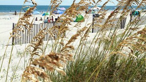 Ein Strand mit einer Holzlattenveranda, Sonnenschirmen und entspannten Menschen.