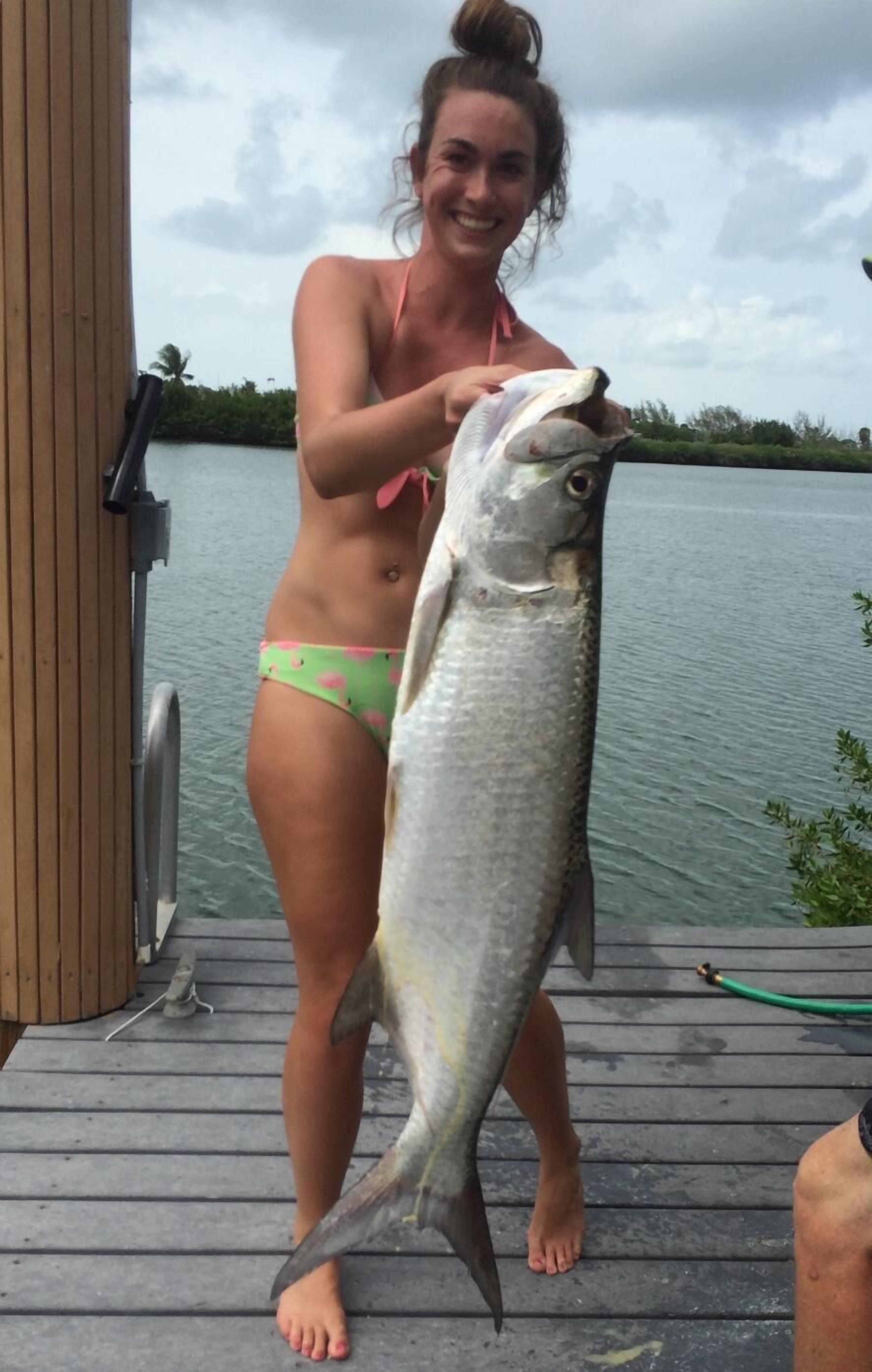 A person standing on a wooden deck holding a large fish.