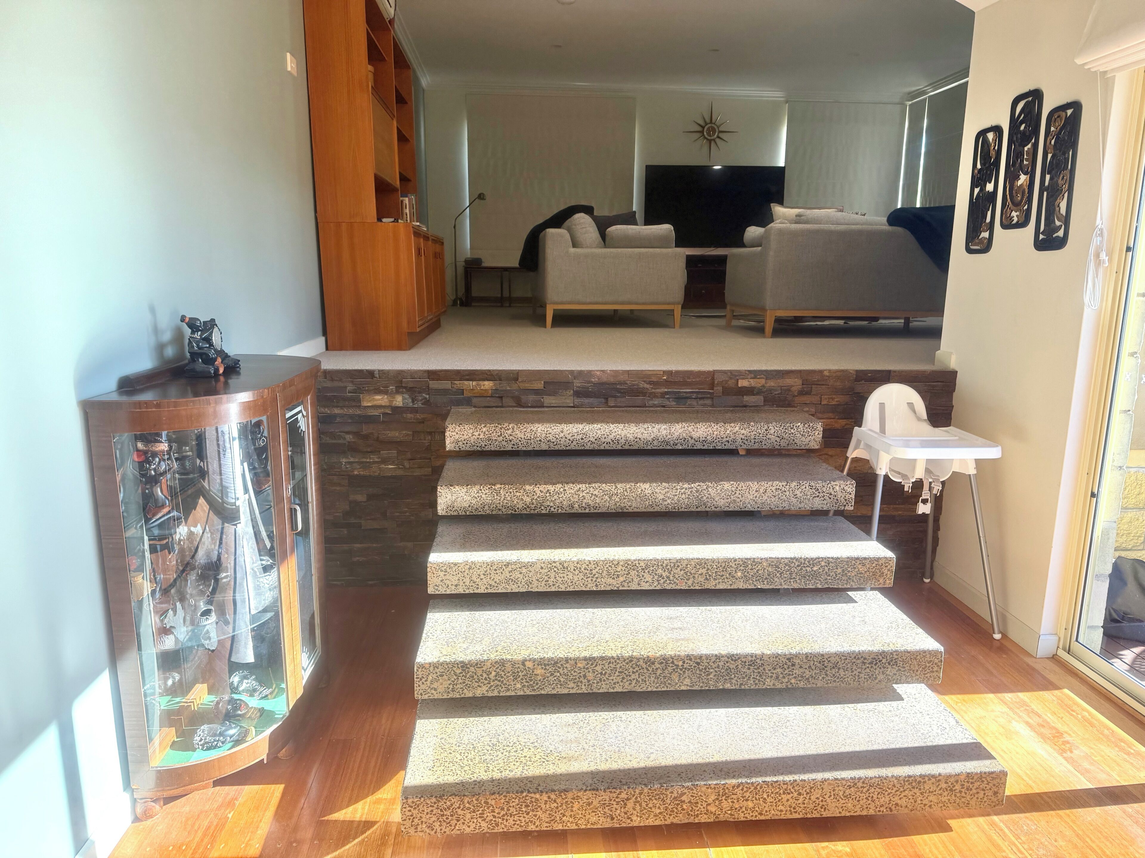 A staircase with a modern design, leading to a living area with a sofa and TV.