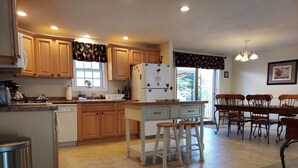 A kitchen with wooden cabinets, a white refrigerator, a sink, and a dining area with wooden chairs and a table. - Spacious vacation house with game room close to North Conway and outlets. (Madison)