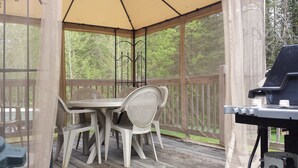 A covered outdoor area with a table and chairs, a grill, and a wooden deck. - Spacious vacation house with game room close to North Conway and outlets. (Madison)