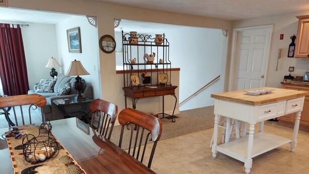 A dining area with a wooden table, chairs, and a decorative rug. There is a kitchen area with a white table and a wooden counter. - Spacious vacation house with game room close to North Conway and outlets. (Madison)