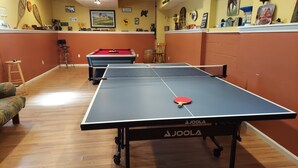 A ping pong table with a paddle, a pool table, and various wall decorations in a room with wooden flooring. - Spacious vacation house with game room close to North Conway and outlets. (Madison)