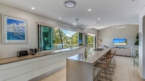 A modern kitchen with a large island, bar stools, and a view of the outdoors. - Paradise@Peninsula Hamilton Island (Hamilton Island)