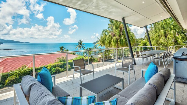 An outdoor seating area with a view of the ocean, a grill, and a red-roofed building in the background. - Paradise@Peninsula Hamilton Island (Hamilton Island)