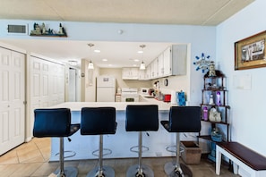 Una cocina con una isla central, taburetes de bar y una estantería decorada con objetos náuticos.