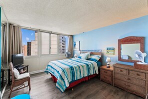 Quarto de hotel com cama, escrivaninha, televisão, poltrona, cômoda e uma grande janela.