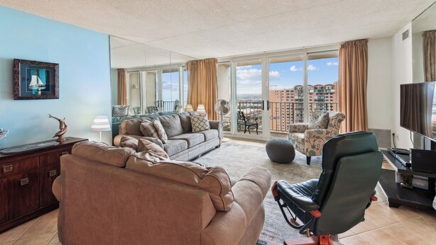 Un salon spacieux avec un grand canapé, un fauteuil noir, une télévision et un balcon offrant une vue sur la ville.