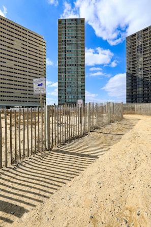 Un sendero arenoso que lleva a una zona vallada con edificios modernos al fondo.