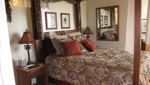 Un lit à baldaquin avec une couvre-lit à motifs, deux lampes de chevet, une table de chevet avec une boîte à mouchoirs et des tableaux encadrés accrochés au mur.