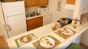 Une cuisine avec des meubles en bois, un réfrigérateur blanc, un four à micro-ondes et un coin repas avec une table mise pour deux personnes.