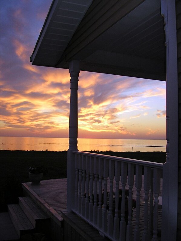 A wooden deck with a railing overlooking a sunset over the ocean.