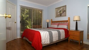 A bedroom with a wooden bed, striped bedding, a red throw, two bedside lamps, a nightstand, and a window with blinds.