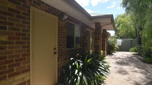 A brick house with a beige door, a window, and a small porch area with plants.