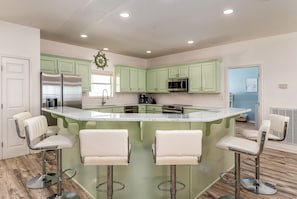 Uma cozinha com armários verdes, uma geladeira de aço inoxidável, micro-ondas e uma ilha grande com banquetas.