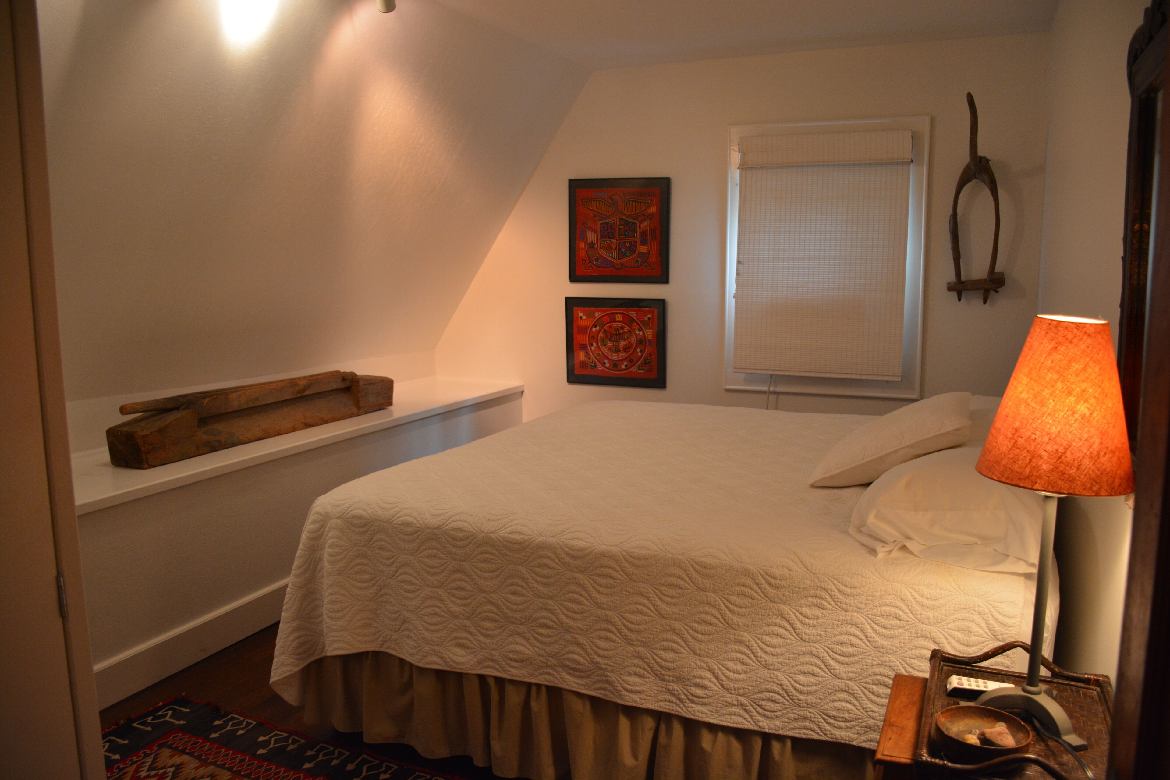 Een slaapkamer met een bed, een nachtkastje, een lamp en twee ingelijste foto’s aan de muur.