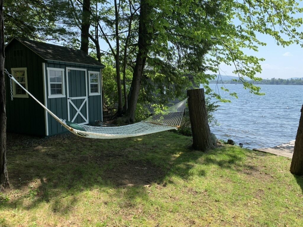 A hammock tied between two trees, a small shed, and a lake.