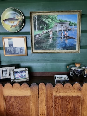 Experience a cozy retreat with a rustic charm, featuring a wooden wall adorned with a serene landscape painting, a family photograph, and a decorative plate.