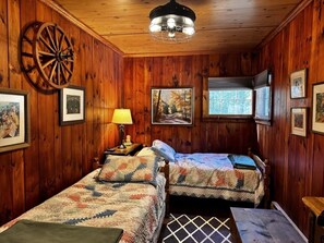 A wooden cabin room with two beds, a large wheel, framed pictures, and a window. - Lakefront House & Cottage ~ walk-in beach, hammock, canoe, kayaks and sunsets (Kattskill Bay)