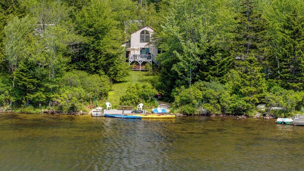 Une maison entourée d’une forêt dense, un quai avec un kayak et un petit bateau.