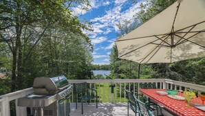 Une terrasse avec un barbecue, une table d’extérieur, des chaises et un grand parasol.