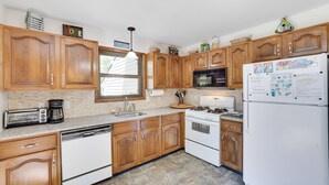 Une cuisine avec des meubles de rangement en bois, un réfrigérateur blanc, une cuisinière, un four à micro-ondes et un lave-vaisselle.