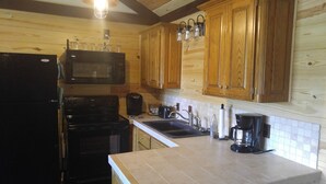 Una cocina con armarios de madera, microondas, estufa, fregadero y cafetera.