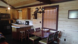 Interior de una cabaña de madera con cocina, mesa de comedor y sillas.