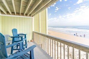 Ein überdachter Außenbereich mit Blick auf den Strand, mit einer Holzterrasse und blauen Adirondack-Stühlen.