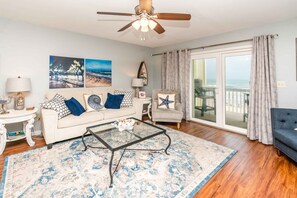 A living room with a sofa, armchair, coffee table, and a view of the beach through a sliding glass door.