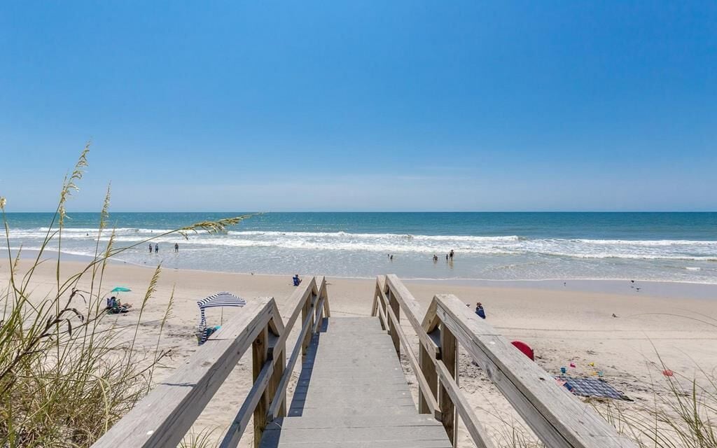 A wooden boardwalk leading to a beach with clear skies and calm waves.