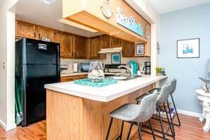 A kitchen with wooden cabinets, a black refrigerator, a bar area with two chairs, and a sign that reads 'Seashore.'