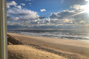 A beach view from a balcony with footprints in the sand. - Surfin' Sunrise - Oceanfront Surf Condo with Pool,  Sleeps 6 (Surf City)