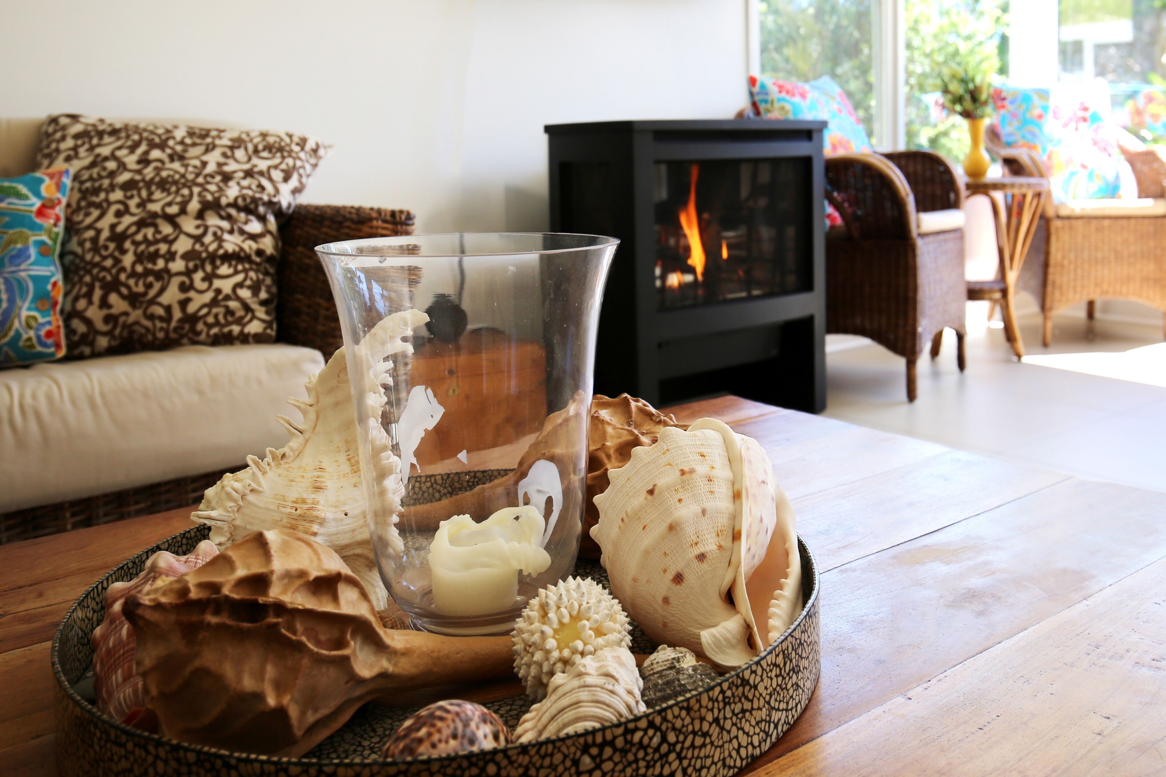 A living room with a fireplace, a glass candle holder with a candle, and decorative seashells on a wooden table.