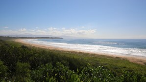 Paesaggio costiero con spiaggia, oceano e montagne lontane sotto un cielo sereno.