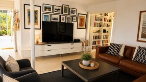 Moderni olohuone, jossa on litteänäyttöinen televisio, kirjahylly, ruskea nahkasohva ja sohvapöytä, jonka päällä on kasvi.