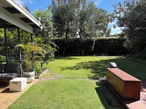 A well-maintained garden with a lawn, a wooden deck, and a seating area with a sofa and a planter.