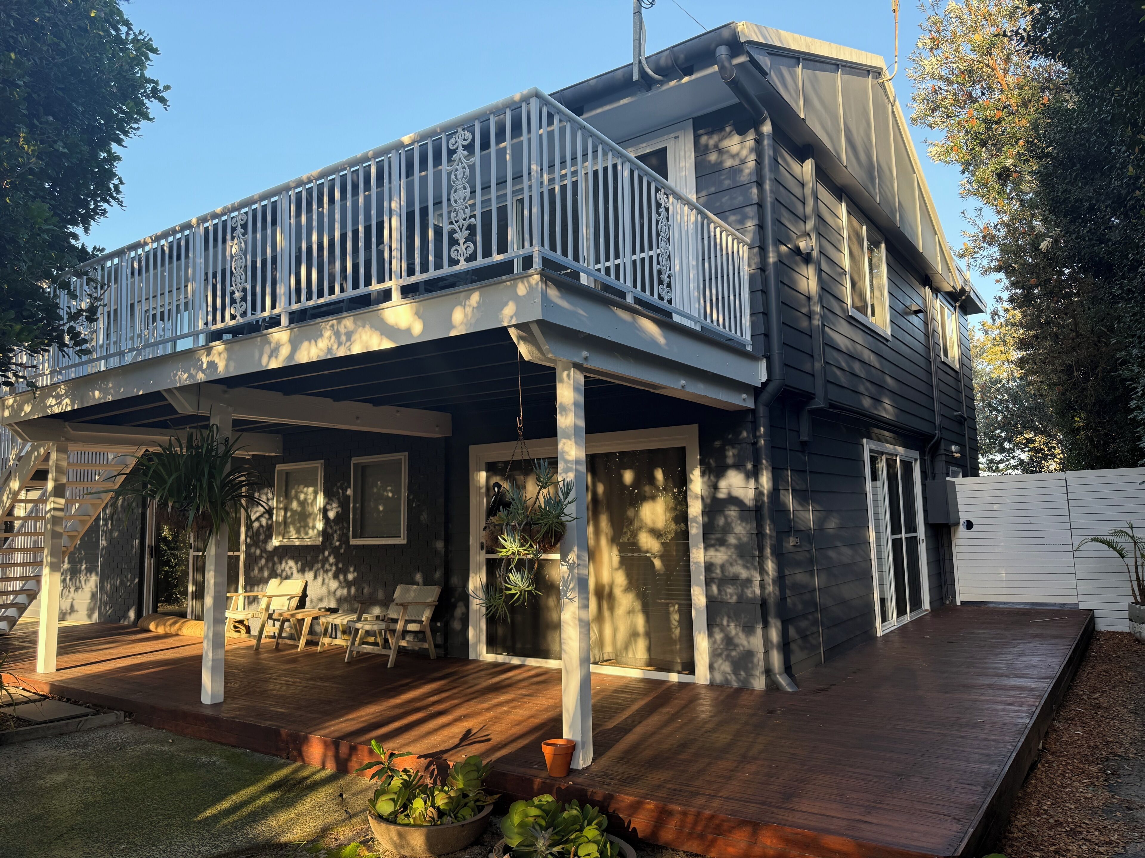 A two-story house with a covered porch, outdoor seating, and potted plants.