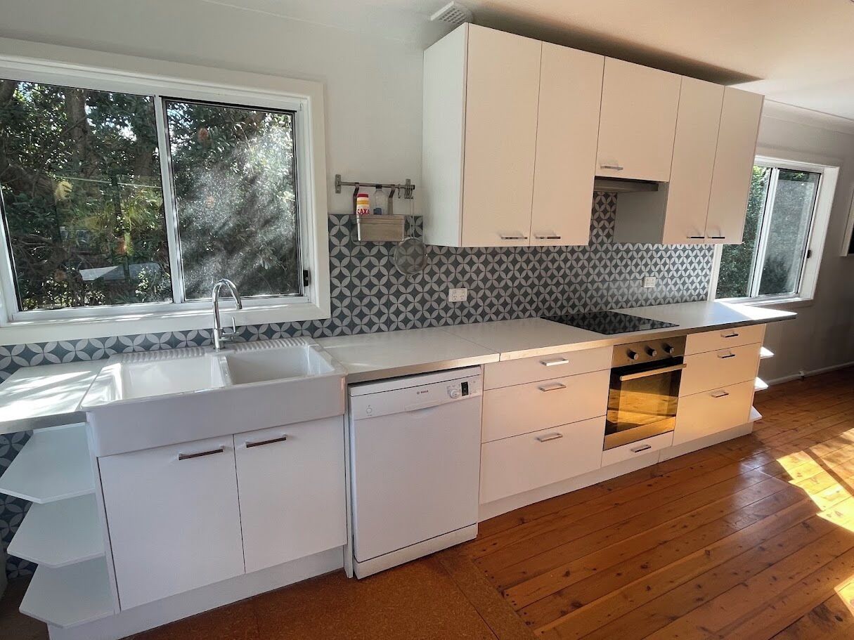 Una cocina moderna con armarios blancos, lavavajillas, horno y ventana que deja entrar luz natural.