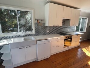 A modern kitchen with white cabinetry, a dishwasher, an oven, and a window providing natural light.